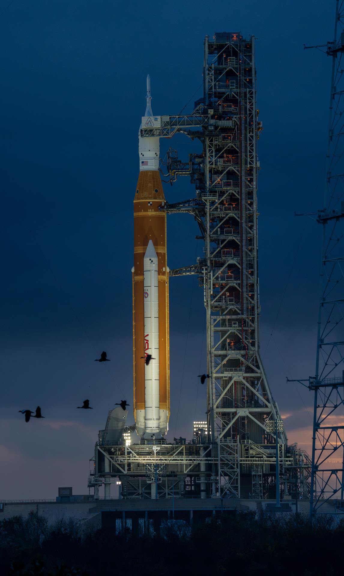 This image shows a sunset of NASA’s SLS (Space Launch System) and Orion spacecraft at NASA’s Kennedy Space Center. NASA's massive Crawler-Transporter, upgraded for the Artemis program, carried the powerful SLS rocket and Orion spacecraft on the Mobile Launcher from the Vehicle Assembly Building to Launch Pad 39B at Kennedy Space Center in preparation for the Artemis II mission.